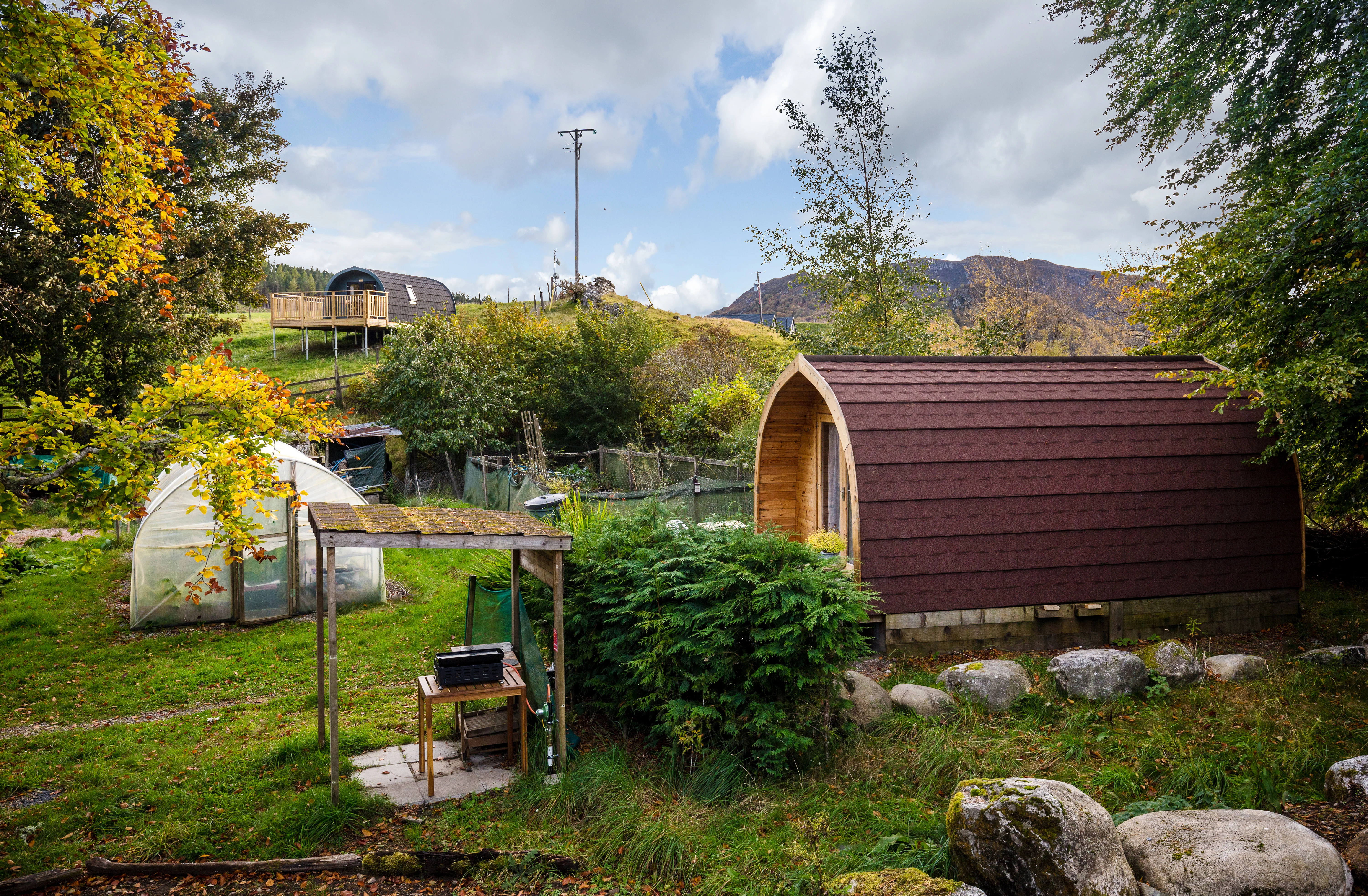 Muckle Meadow Pod at Glentruim — burgundy arched glamping pod in an autumnal croft with polytunnel, Cairngorms behind